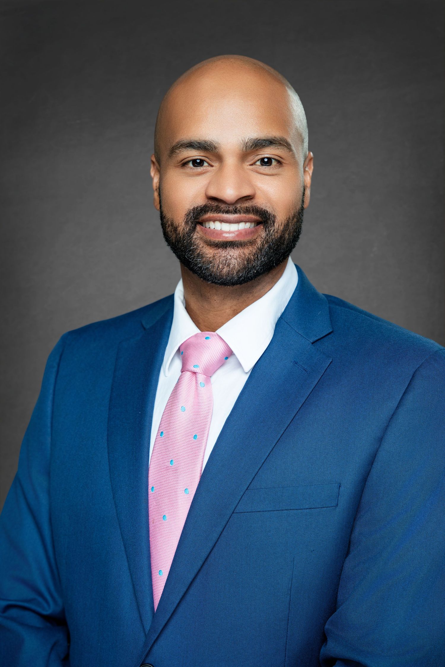 Professional headshot series showing a person in a navy blue suit and pink tie against a dark gray background.