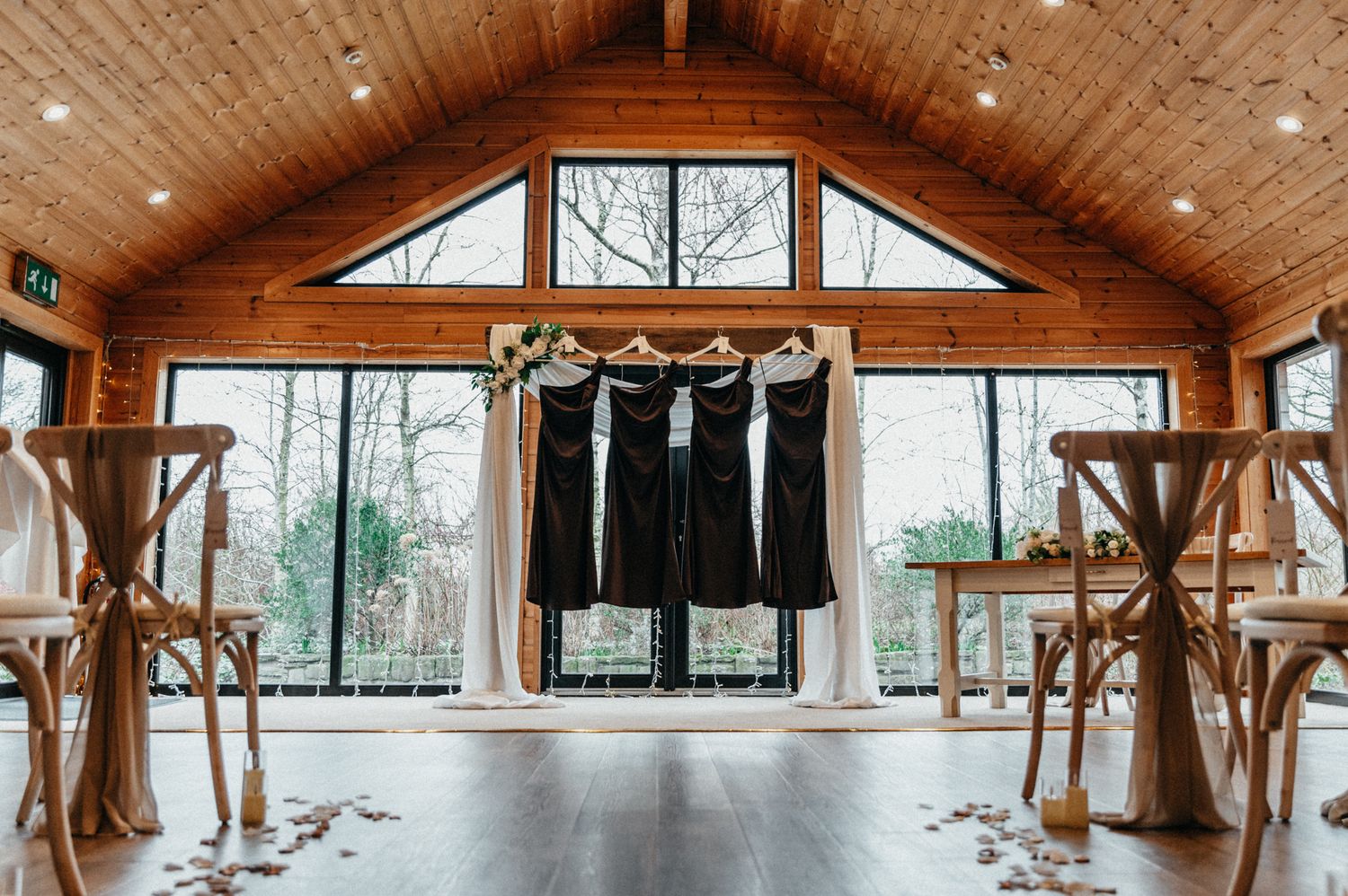 Rustic wooden event venue interior with vaulted ceiling, exposed beams, and natural lighting through large windows.
