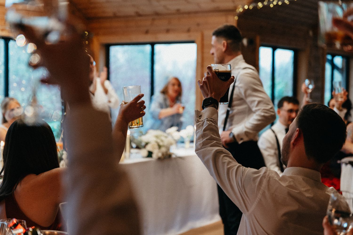 Wedding reception celebration inside a cozy wooden lodge decorated with warm lighting.