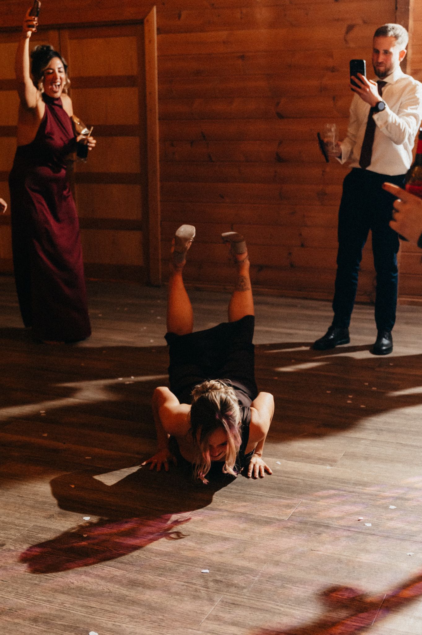 Dancers perform a contemporary routine on a wooden floor in a studio with dramatic lighting and shadows.