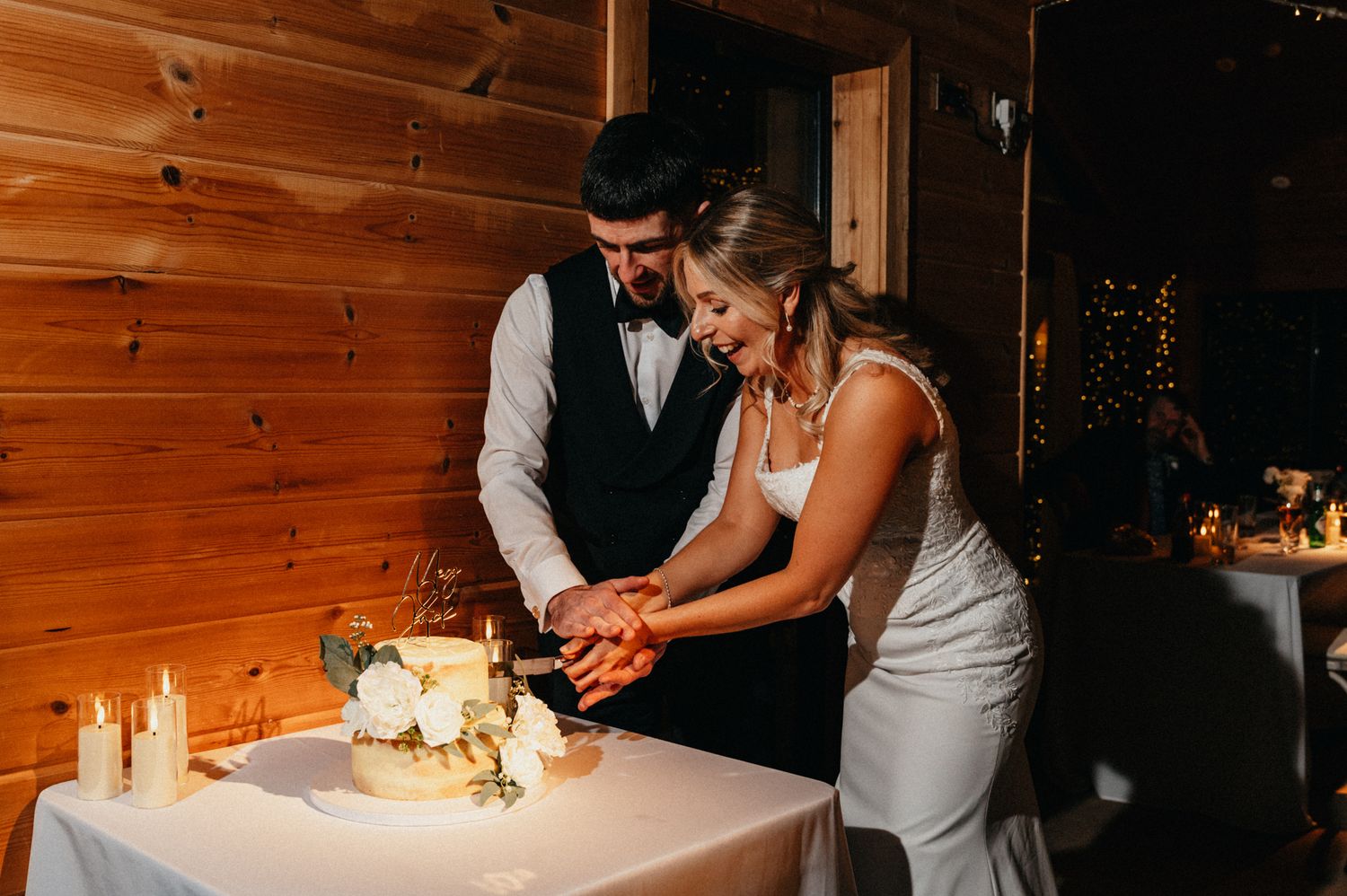 Traditional wedding cake cutting moment in rustic wooden venue with candlelight.