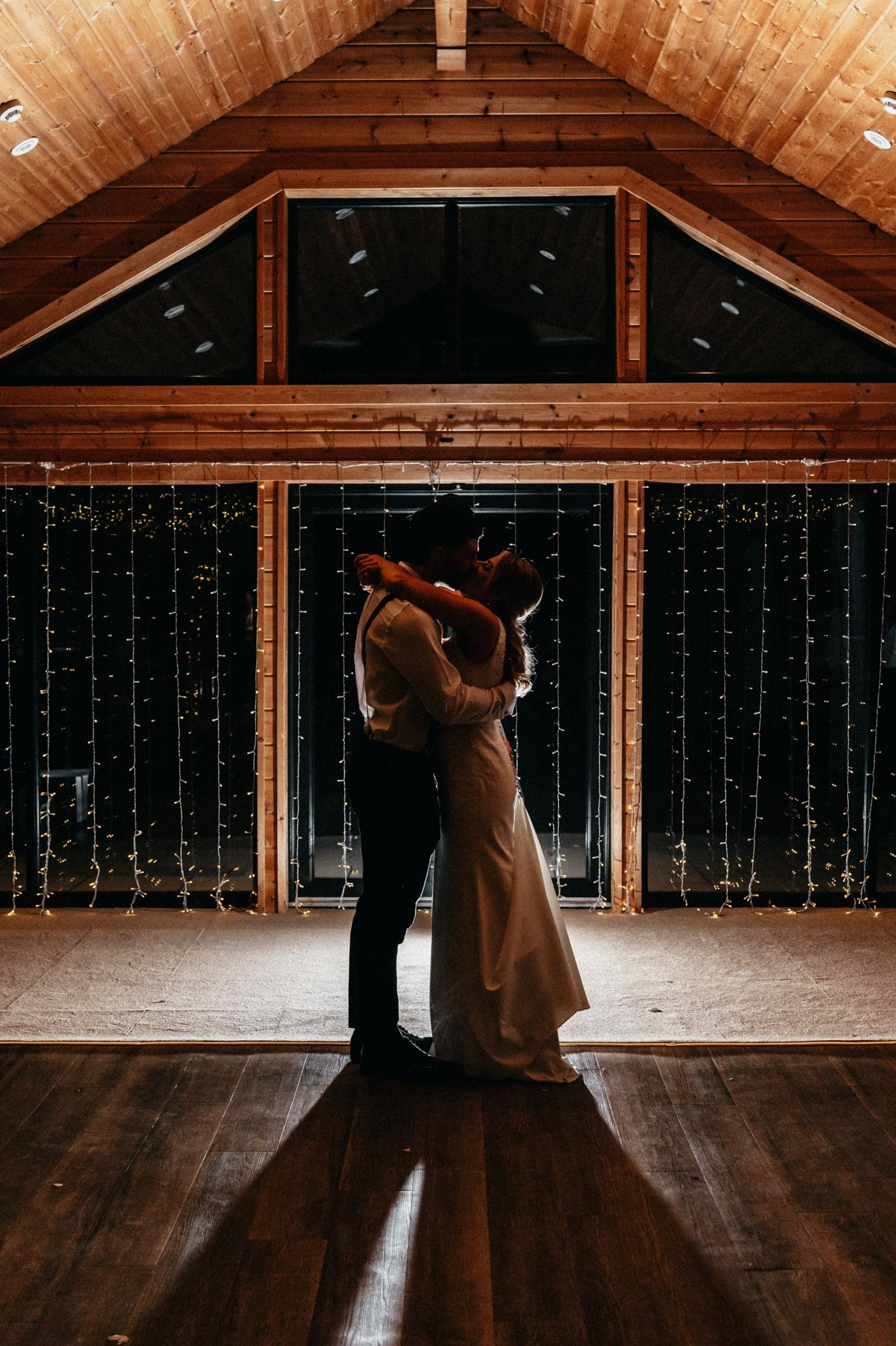 Silhouetted couple dancing in rustic venue with fairy light backdrop.