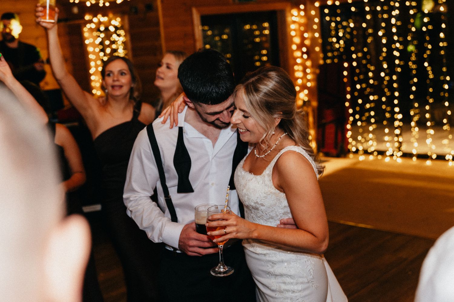 Romantic moment during wedding reception with string lights creating warm ambiance in background.