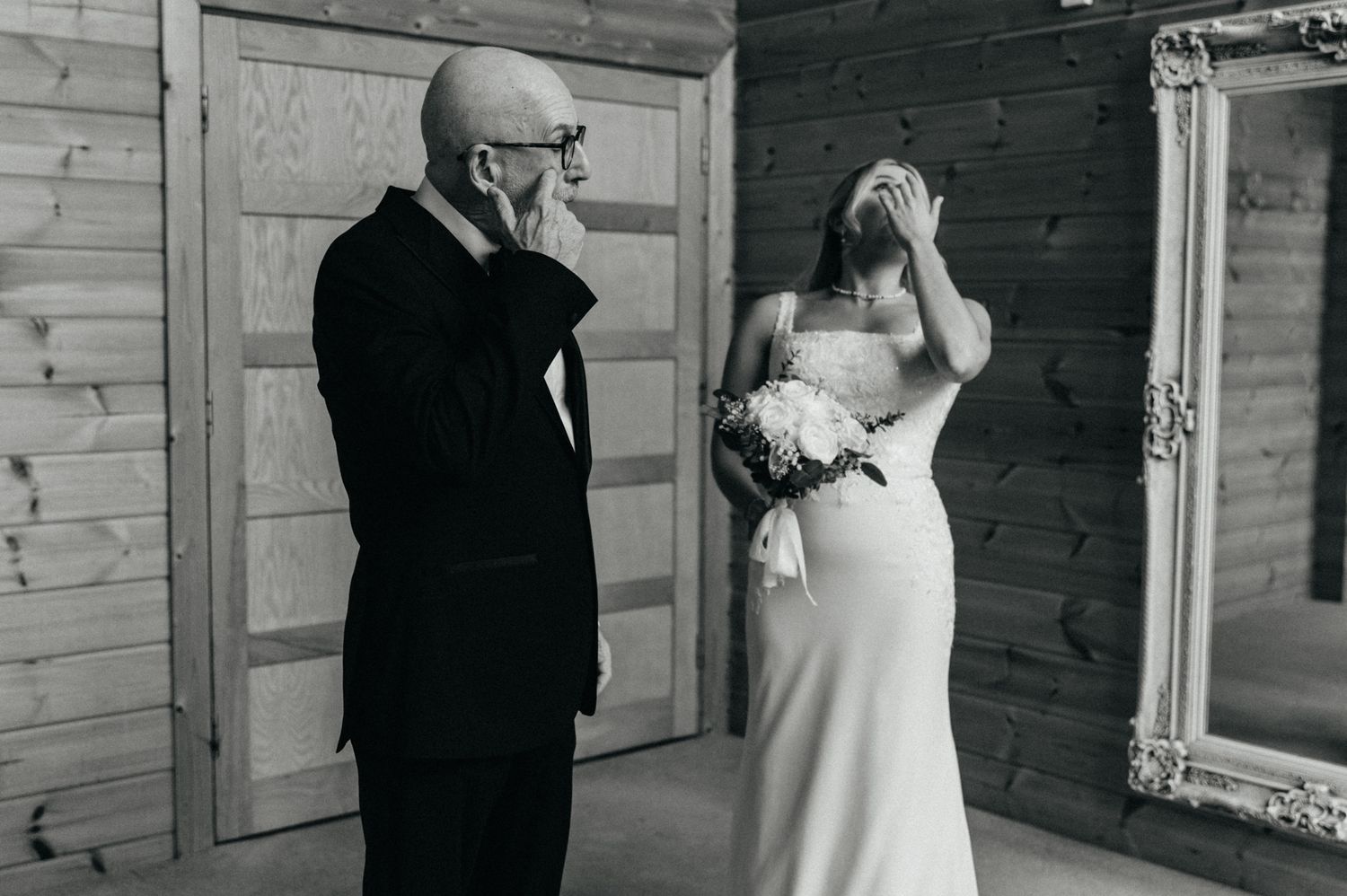 First look moment captured between couple in formal wedding attire against wooden wall backdrop.