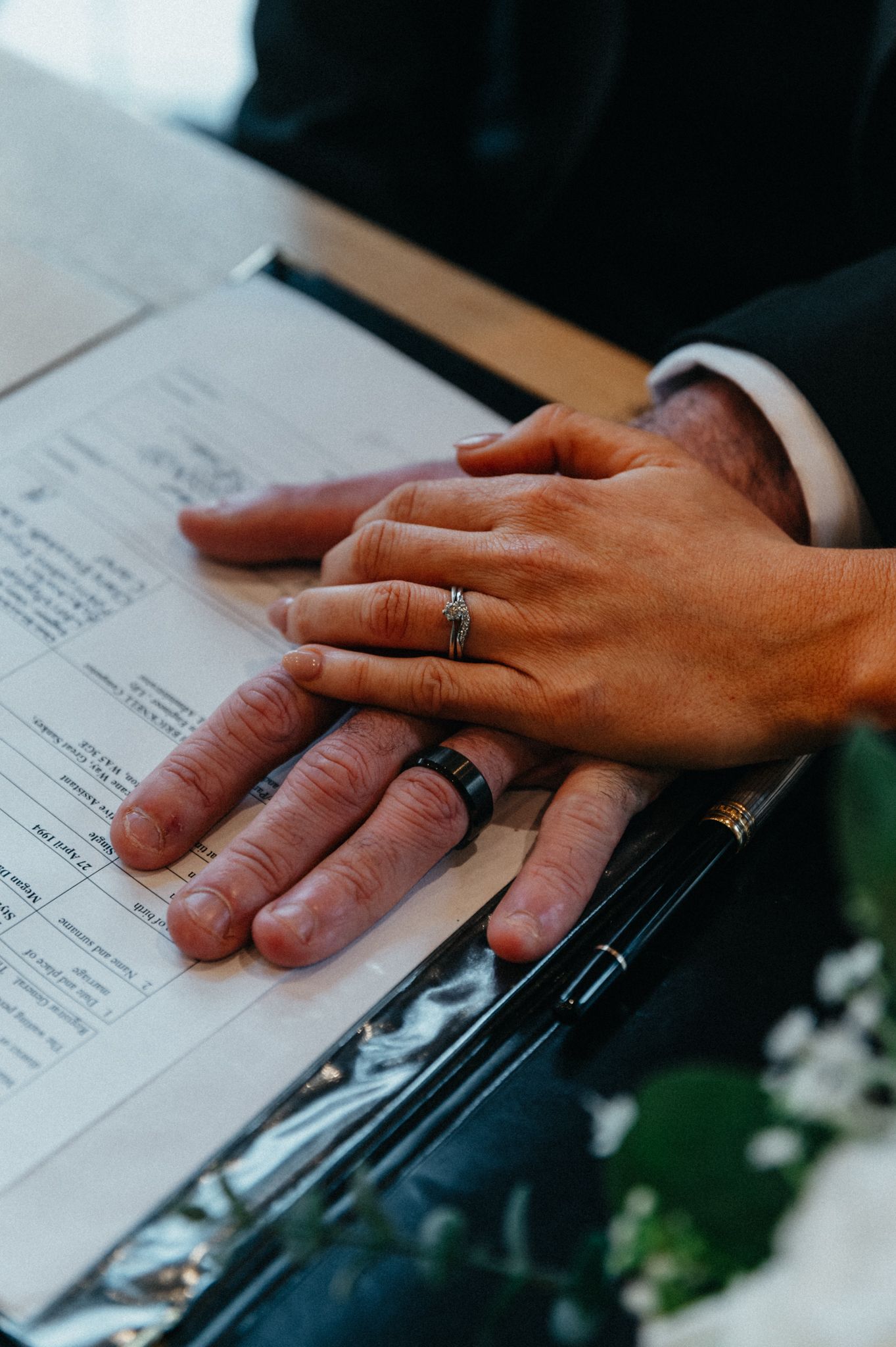 Close-up view of hands with wedding rings resting on papers during a document signing ceremony.