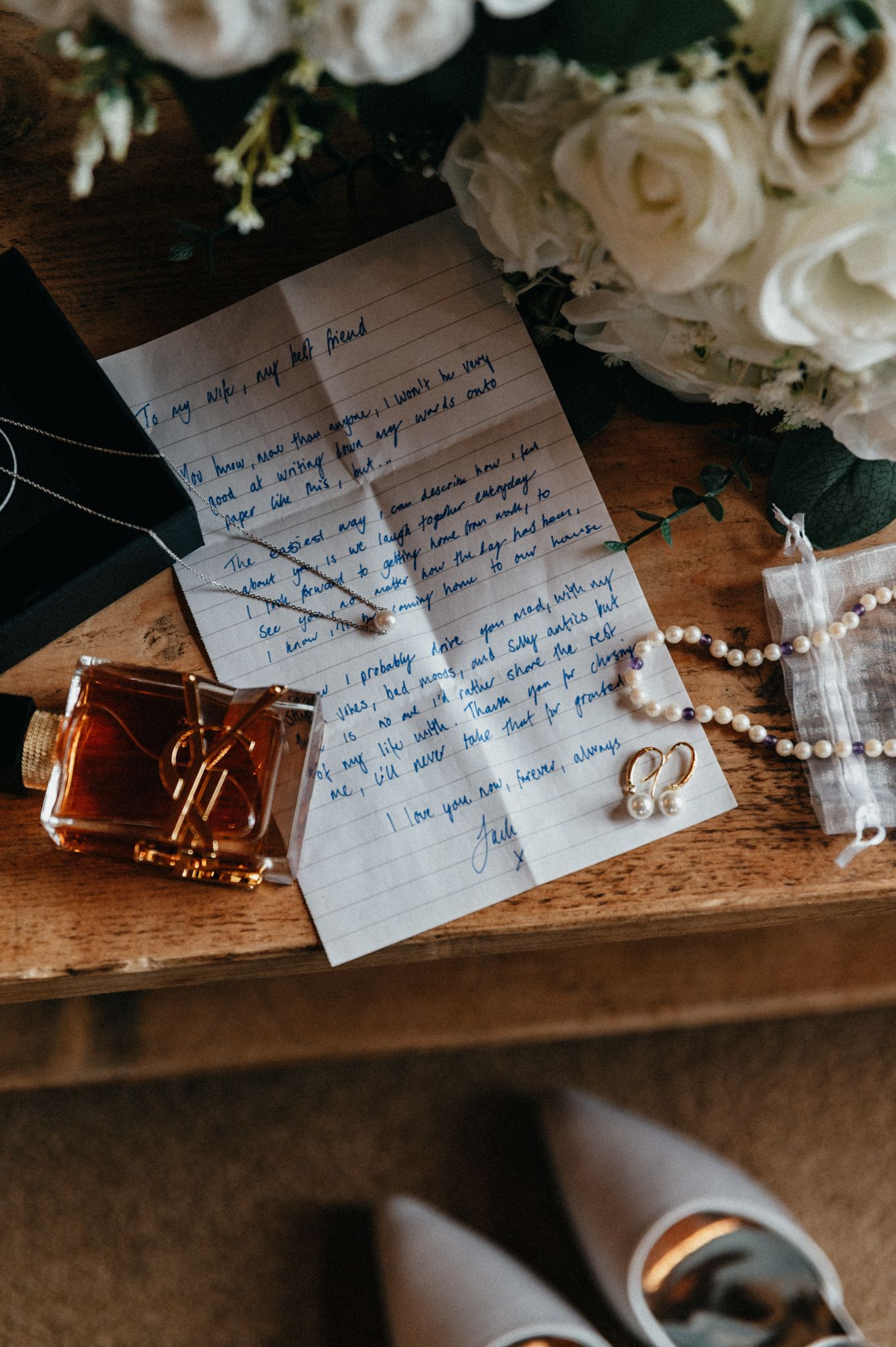 Handwritten wedding vows on blue paper with white roses and pearl decorations on a rustic wooden surface.