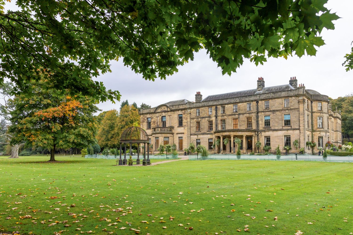Panoramic view of a historic stone mansion with manicured lawns and mature trees in a grand estate setting. Beamish Hall Wedding