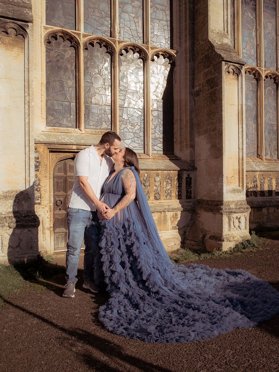 Mum‑to‑be in flowing gown cradling her bump in historic Lavenham St Peter & St Pauls Church, by all scene images photography, Essex, UK