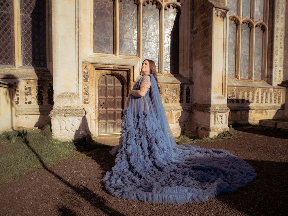 Mum‑to‑be in flowing gown cradling her bump in historic Lavenham St Peter & St Pauls Church, by all scene images photography, Essex, UK