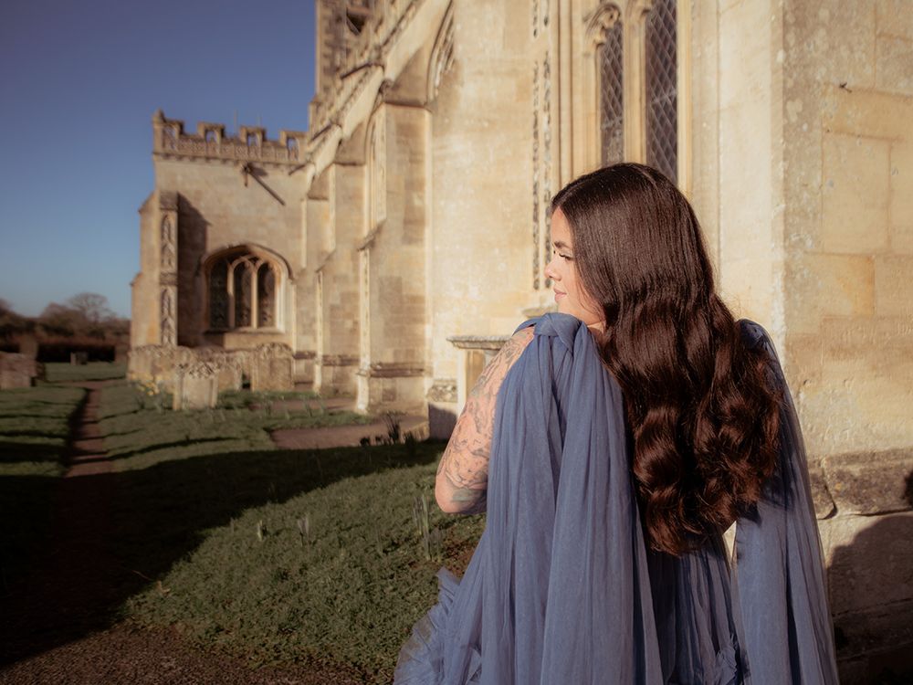 Mum‑to‑be in flowing gown cradling her bump in historic Lavenham St Peter & St Pauls Church, by all scene images photography, Essex, UK