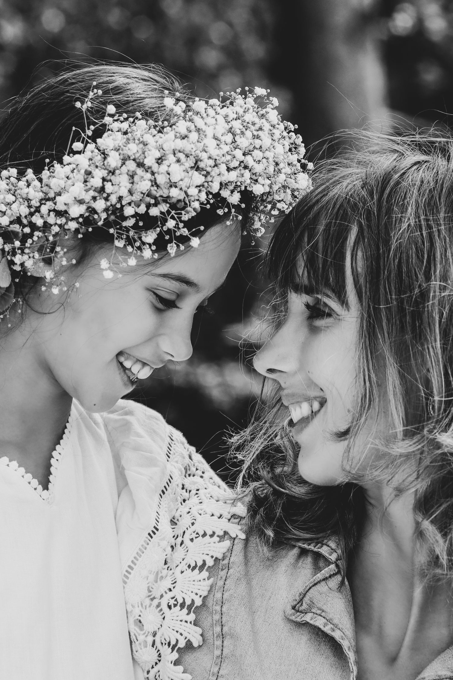 Black and white photo of a girl wearing a floral crown laughing with a woman outdoors.