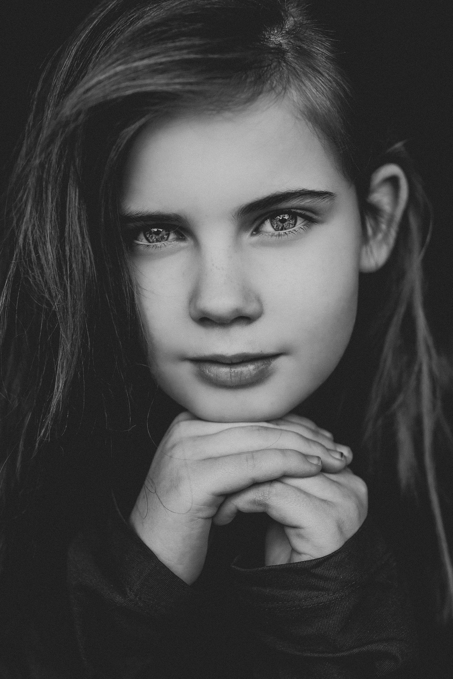 Black and white portrait of a young girl with long hair resting her chin on clasped hands.