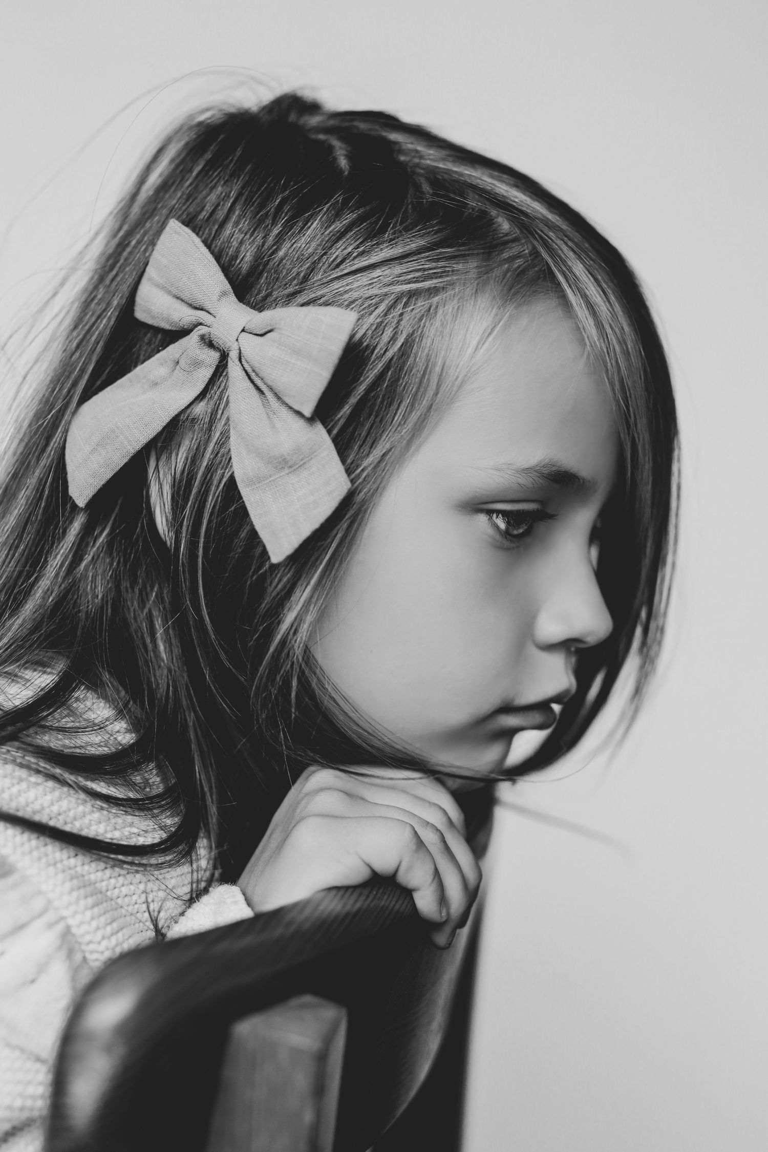 Black and white side profile of a young girl with a bow hair clip resting on a chair.
