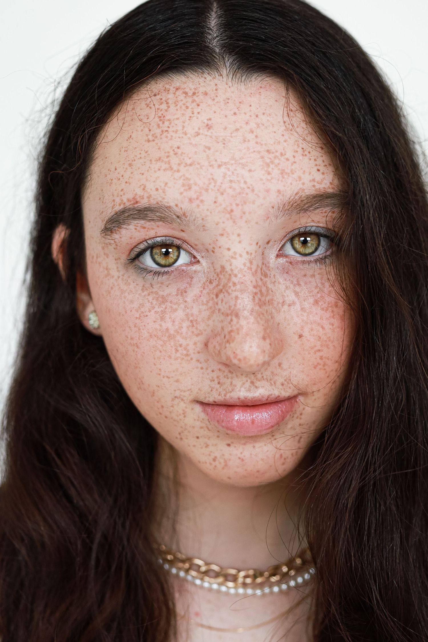 Close-up portrait of a teenage girl with freckles, green eyes, and dark wavy hair.