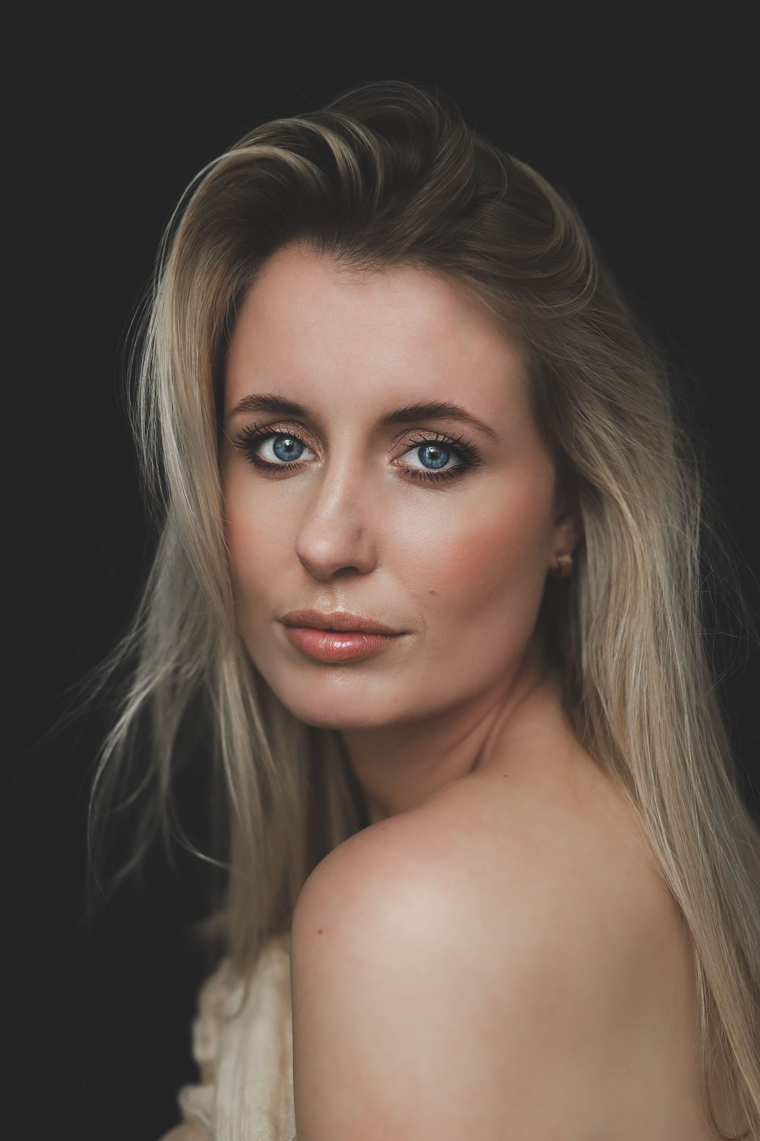 Studio portrait of a blonde woman with blue eyes against a dark background.