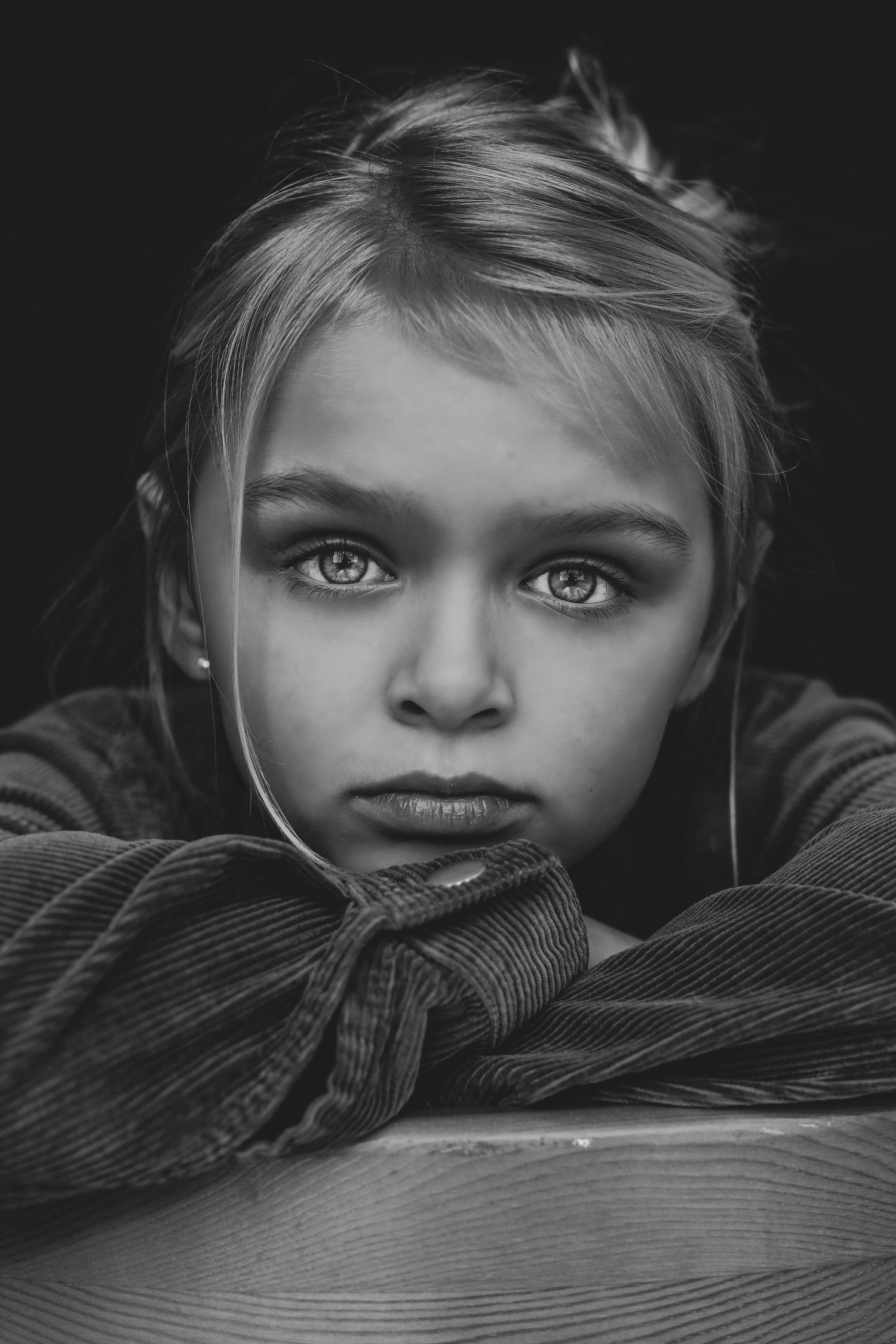 Dramatic black and white portrait of a young blonde girl with intense eyes resting on arms.
