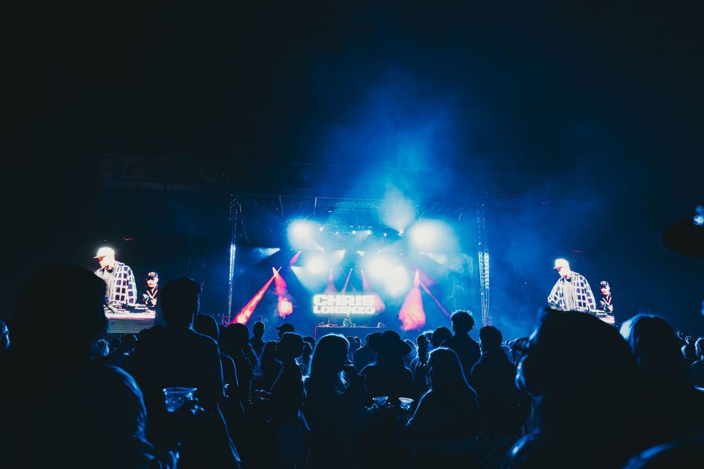 Silhouetted crowd watches a blue-lit concert stage with multiple peaks and lighting effects creating a dramatic atmosphere.