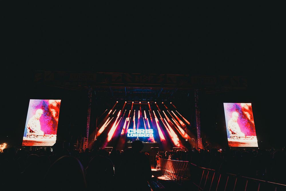 Concert stage illuminated with colorful lights and video screens during a nighttime performance.