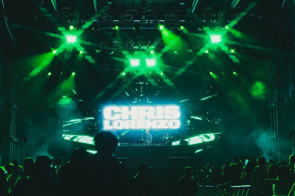 Green laser lights illuminate a dark concert venue with a dramatic stage setup and fog effects during a performance.