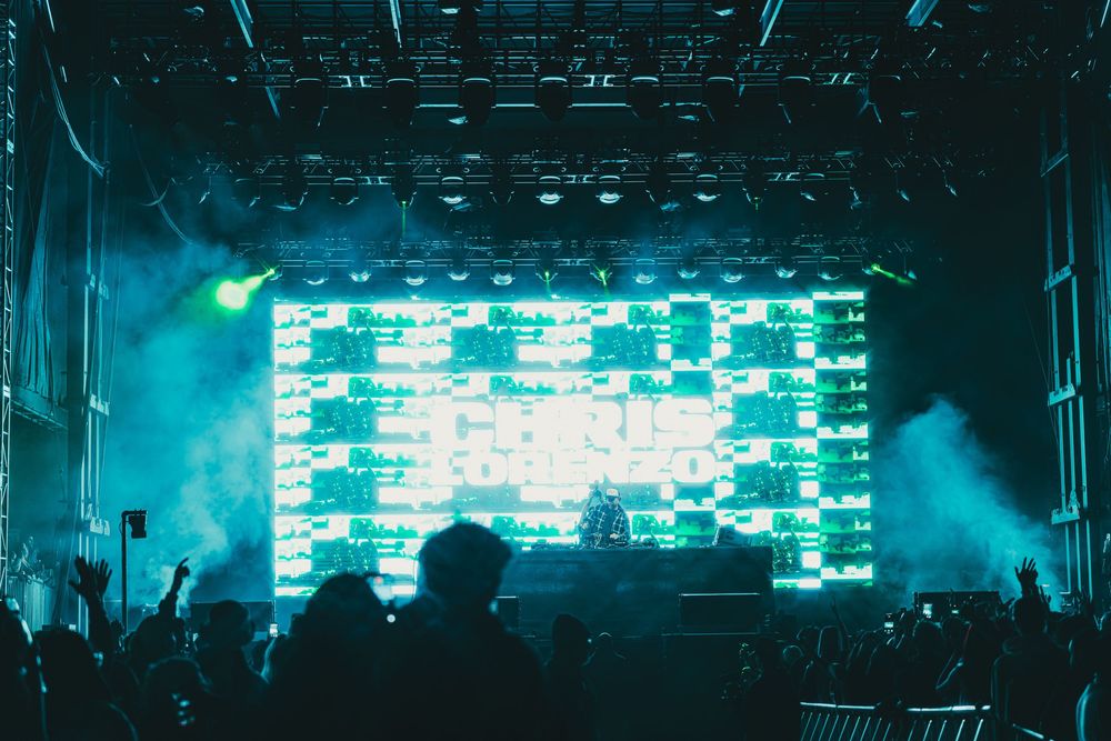 Electronic music festival stage with blue lighting effects and large LED screens displaying digital visuals.