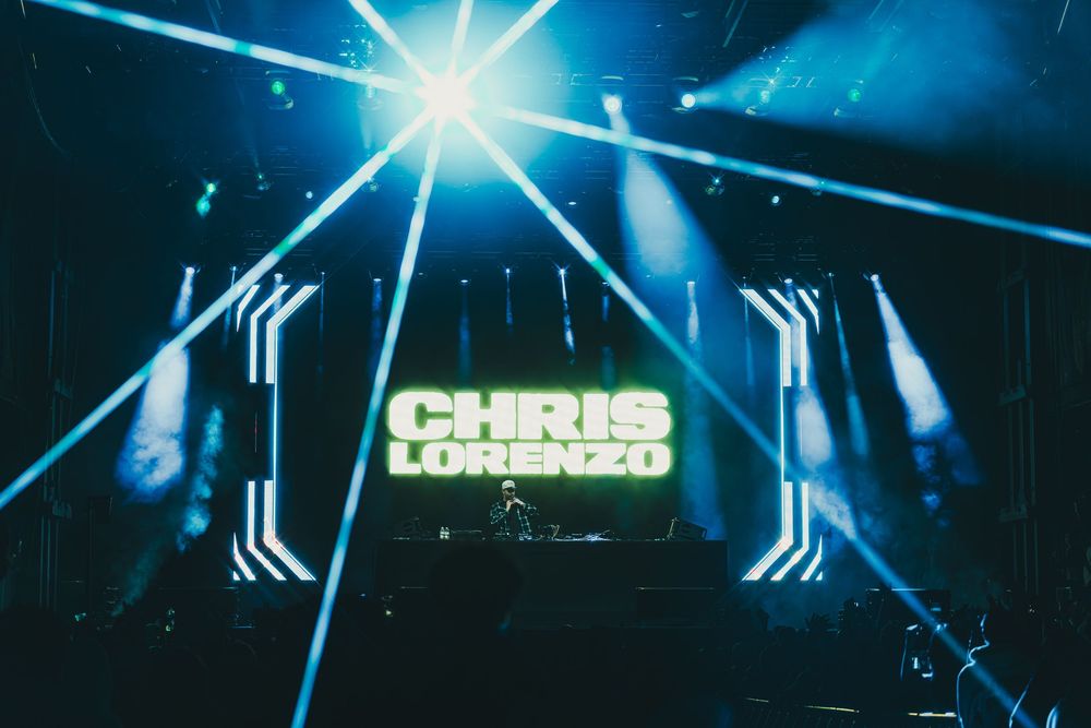 Concert stage with bright blue lighting effects and illuminated 'CHRIS' text display against dark background.