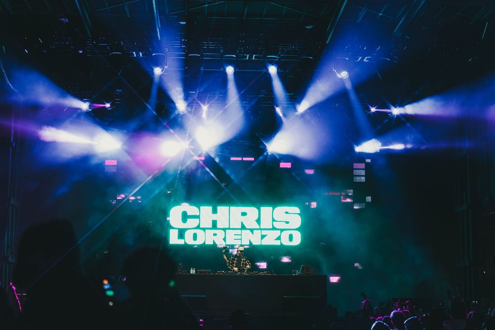 Concert stage lighting effects create dynamic blue and purple beams across a dark venue during a live performance.