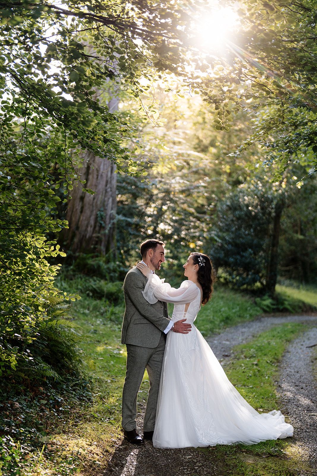 A couple walks along a sunlit wooded path during a wedding photo session at golden hour.