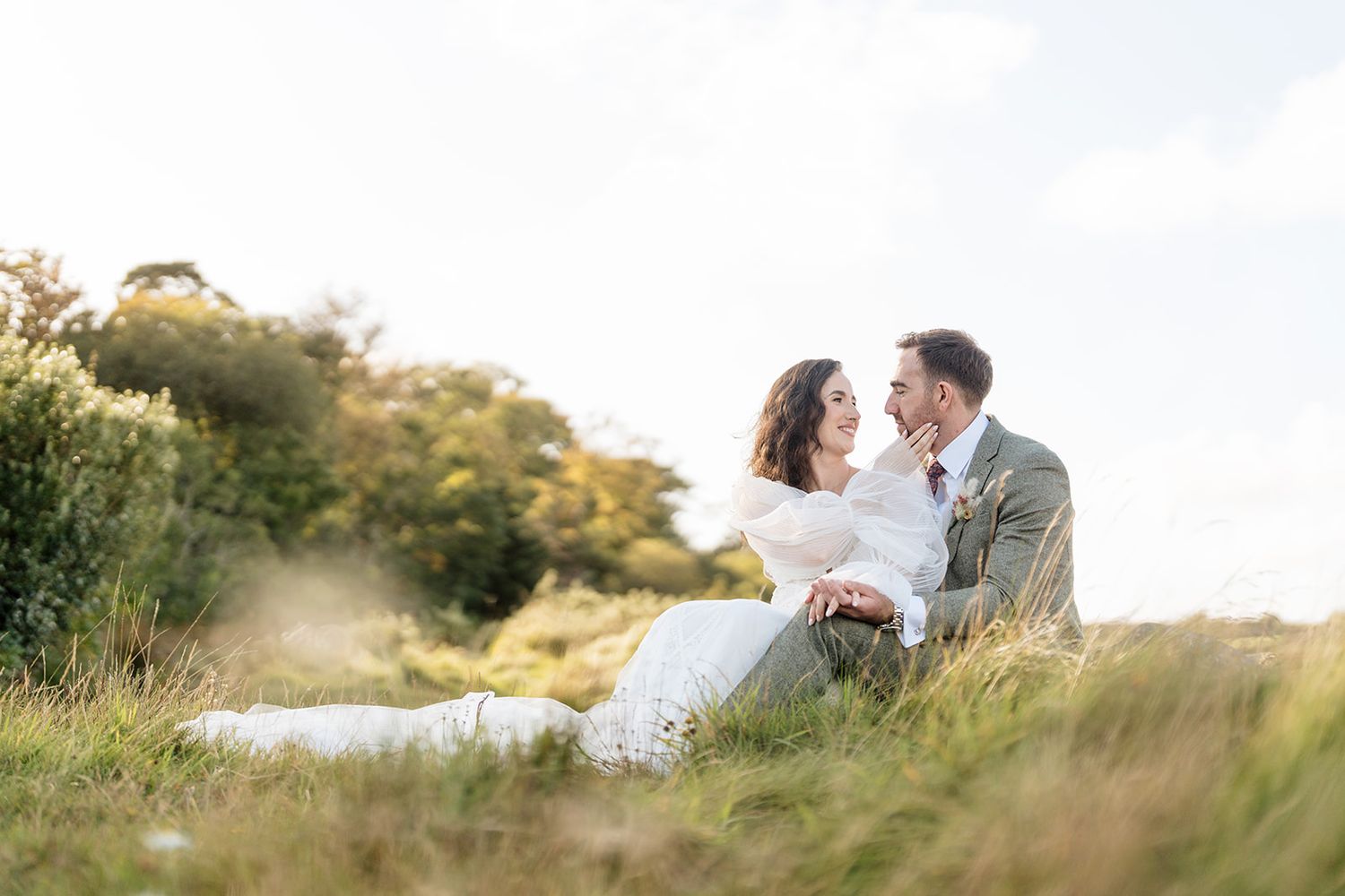 A romantic couple shares a tender moment in a sunlit meadow with golden grass and natural scenery - Inish Beg Wedding Photos by Sarah Kate