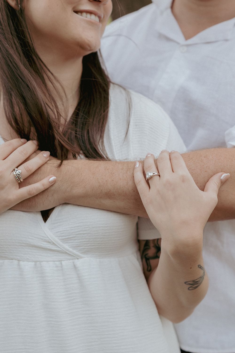 Close-up of hands with wedding rings and tattoo in white clothing.