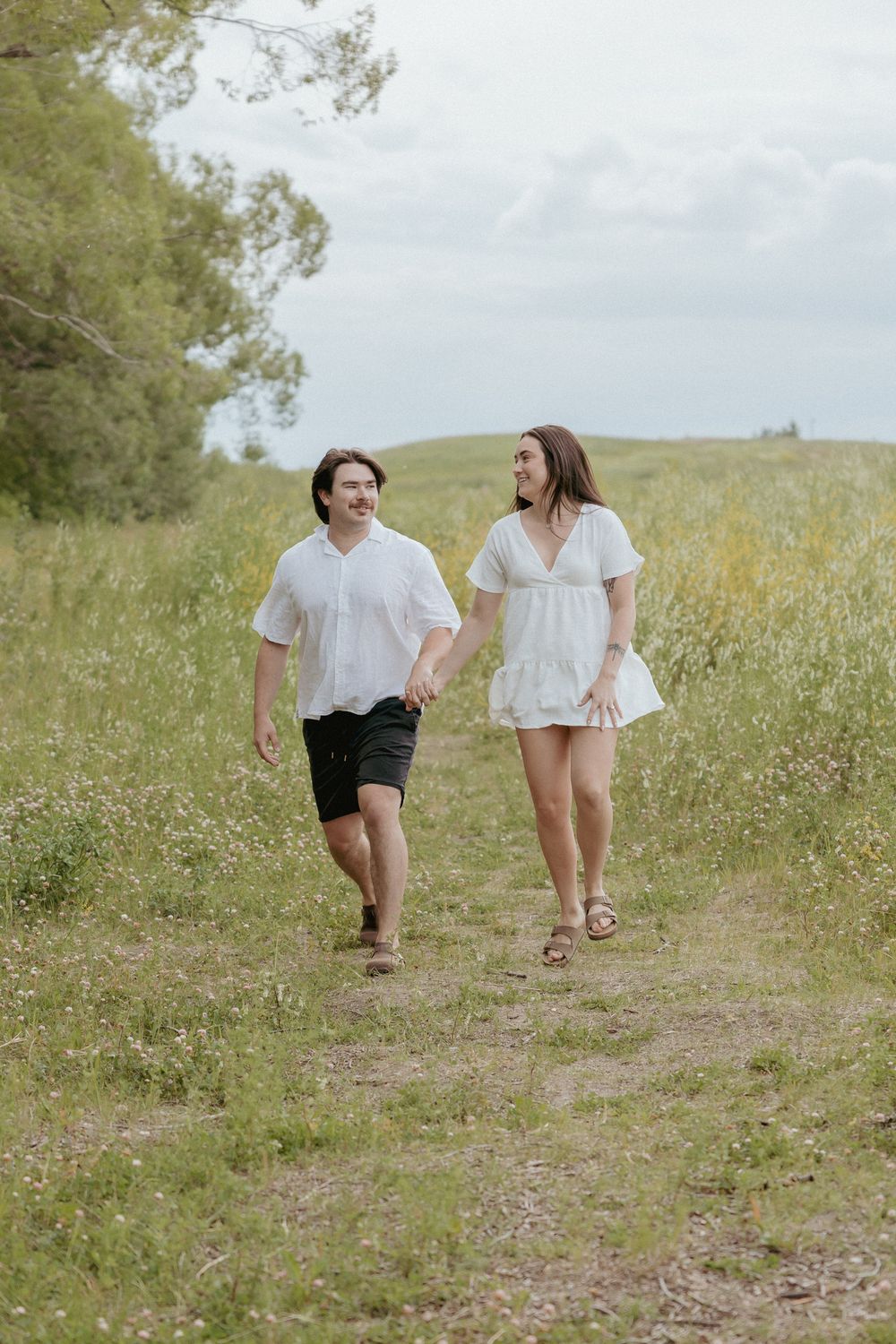Couple walking together through a wildflower meadow wearing coordinated white outfits.