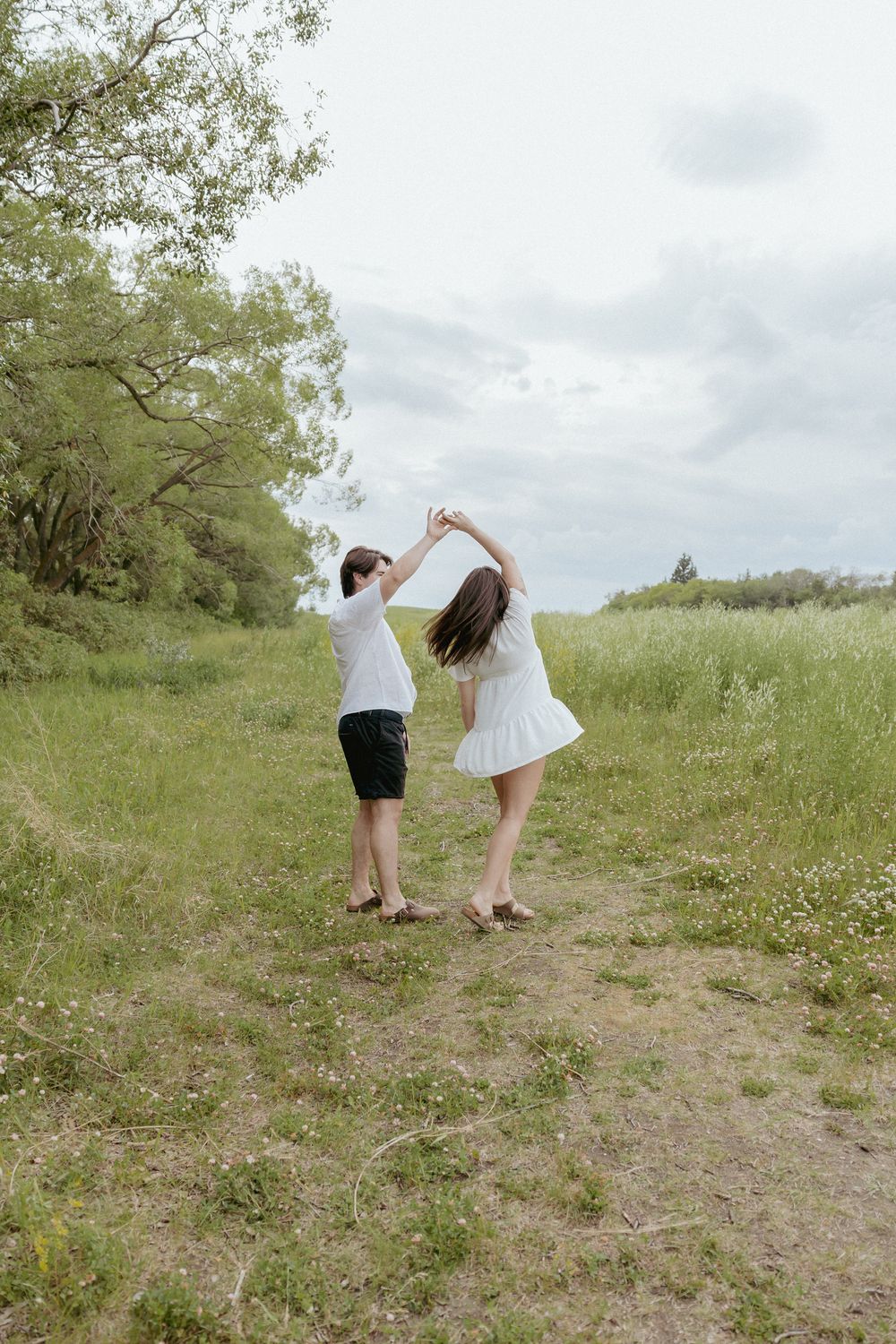 Couple walking hand in hand up a grassy hill on a cloudy day.