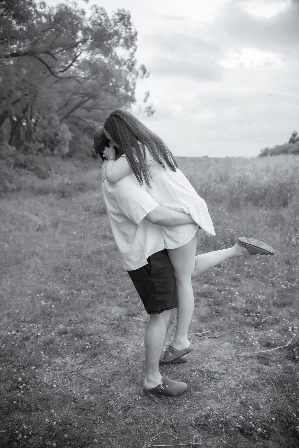 Playful couple dancing and twirling in a meadow wearing white and black outfits.