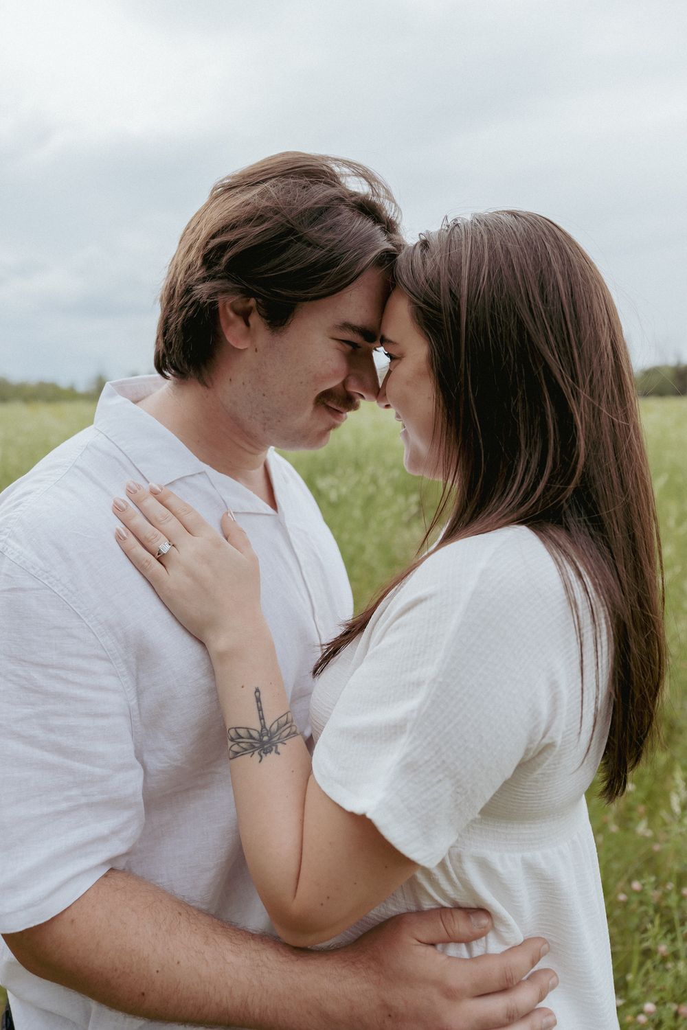 Intimate couple sharing tender moments in a sunny meadow wearing white.