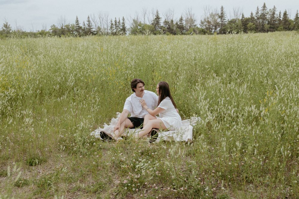 Wide landscape view of couple sitting in a peaceful meadow surrounded by nature.