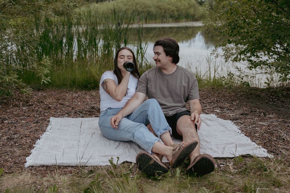 Couple sharing a relaxed moment on a picnic blanket by the water.