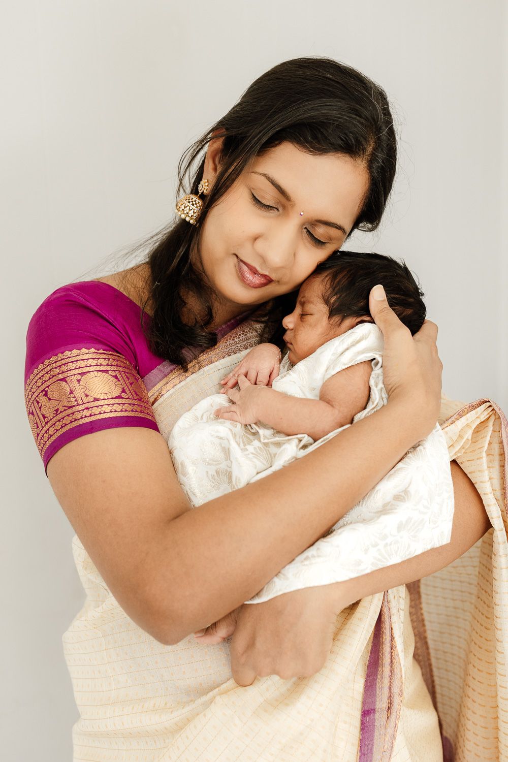 a mom wearing traditional Indian costume cuddles her baby at their in-home baby photography session