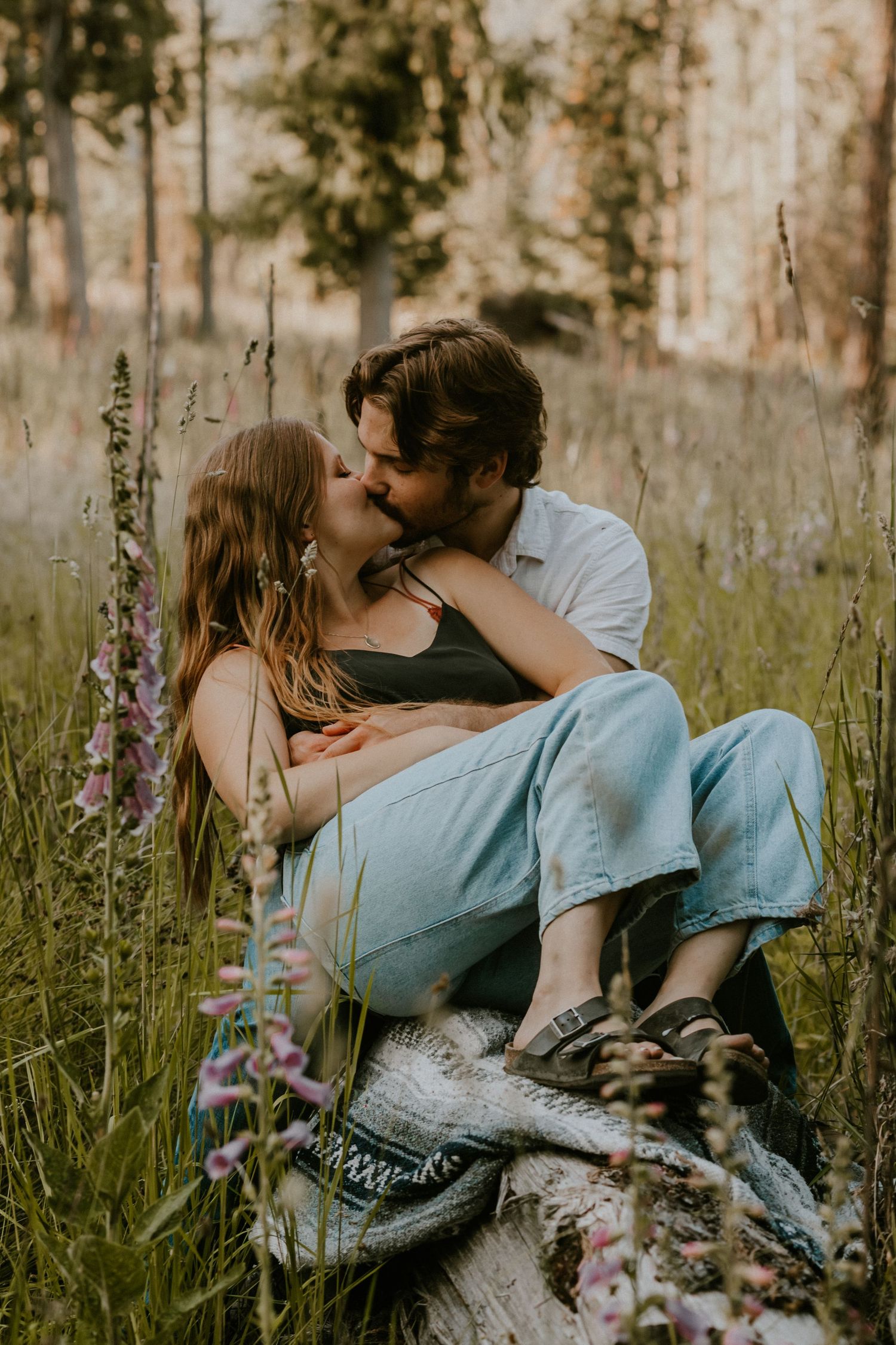 A couple shares an intimate moment while sitting in a wildflower meadow on a sunny afternoon.