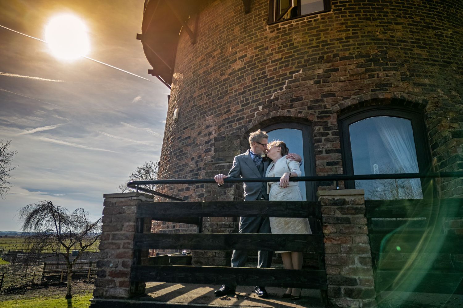 Bride and groom Dorothy and John kissing on the windmill balcony at Windmill Farm in Burscough with warm afternoon sun and lens flare.