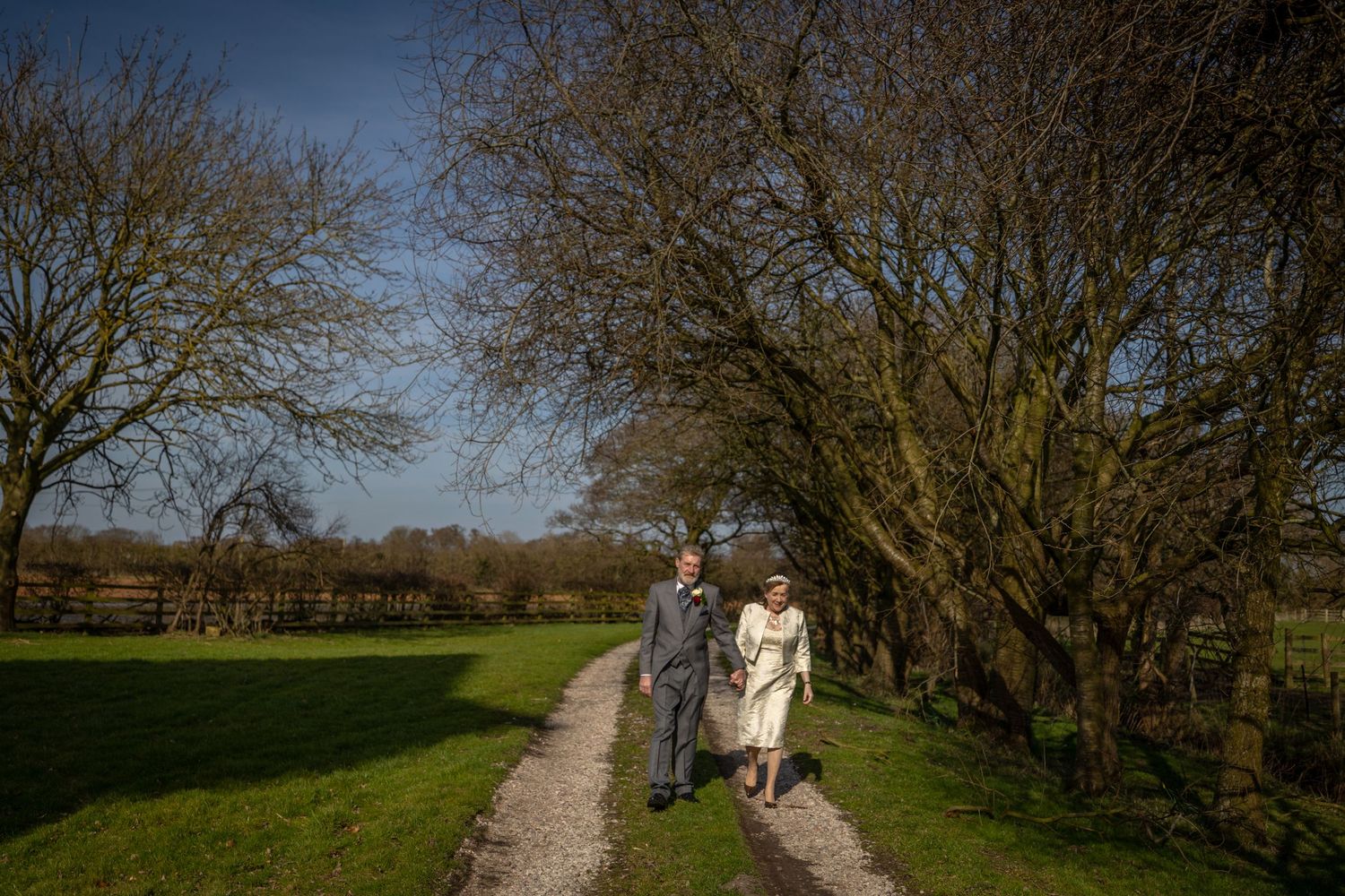 Bride and groom walking hand in hand along a country track at Windmill Farm in Burscough after their wedding ceremony.
