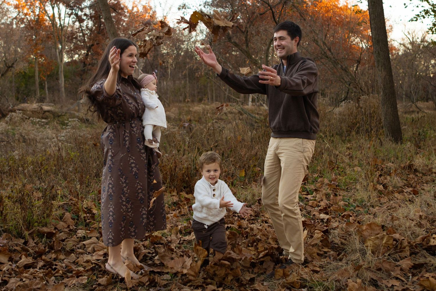 A group sits together on grass in a casual outdoor setting with autumn trees in the background.