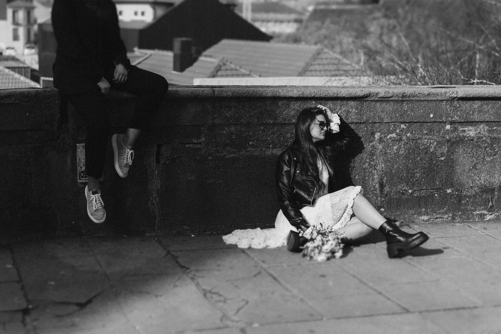 A black and white artistic photo showing feet and shadows on a sidewalk with scattered objects.
