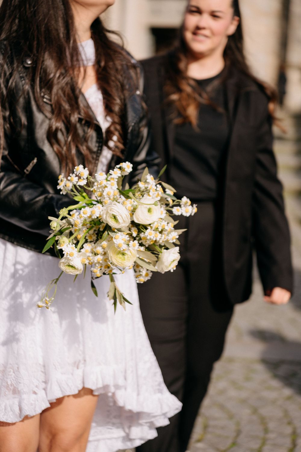 A white lace dress and delicate floral bouquet captured in warm sunlight against stone architecture.