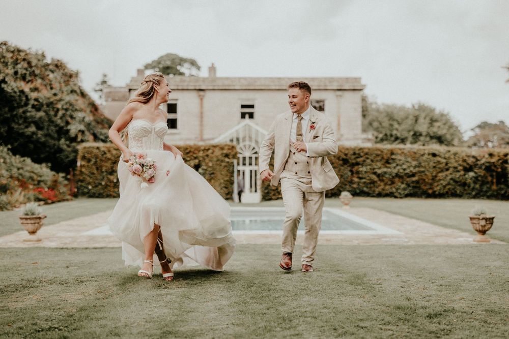 Wedding couple and their guests playfully toss flower petals in the air during an outdoor celebration on a sunny day.
