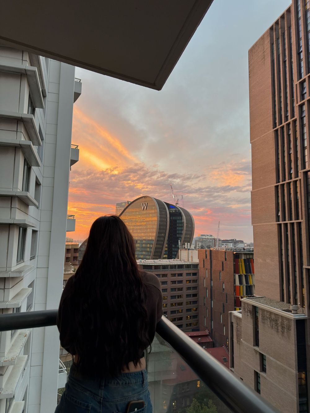 A young woman looking off a balcony into the sunset