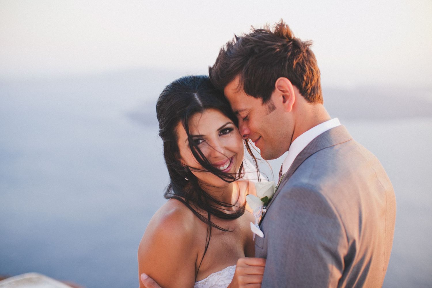 bride and groom on top of cliff at sunset in santorini, greece