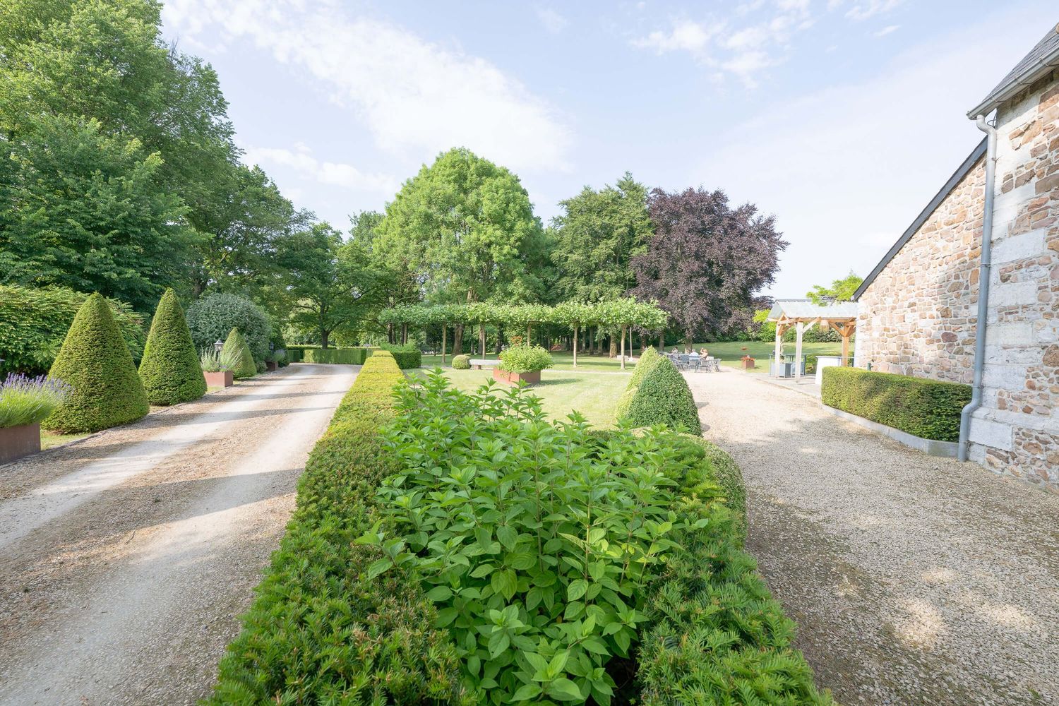 Panoramic view of a winding gravel path through lush green countryside with stone buildings in the distance.