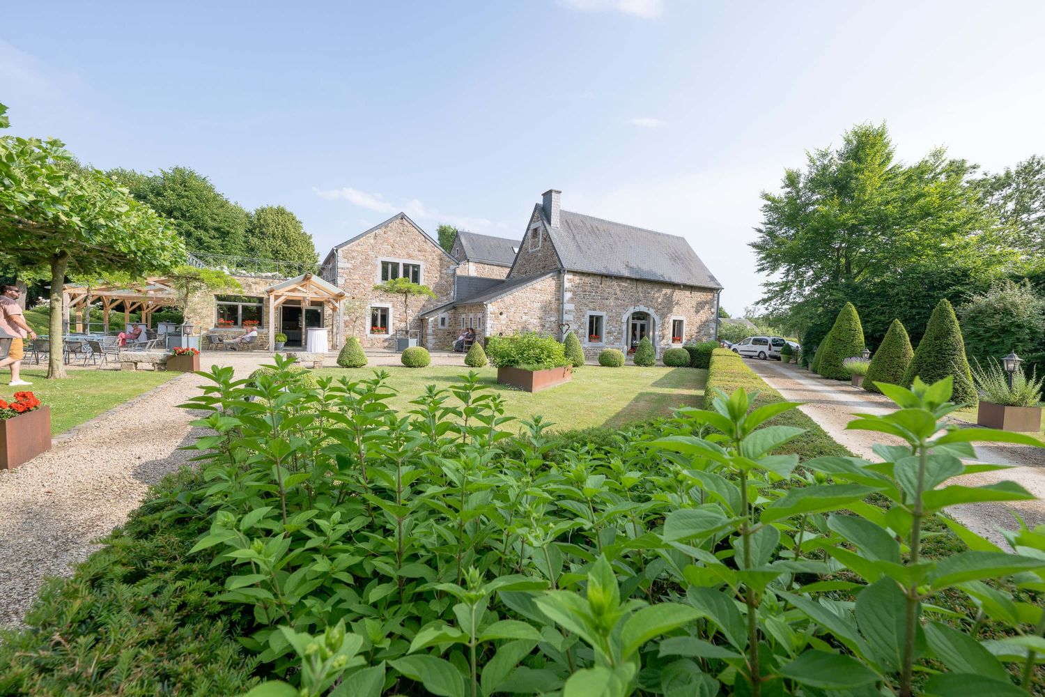Scenic view of a lush green garden path leading to stone houses and manicured hedges on a sunny day.