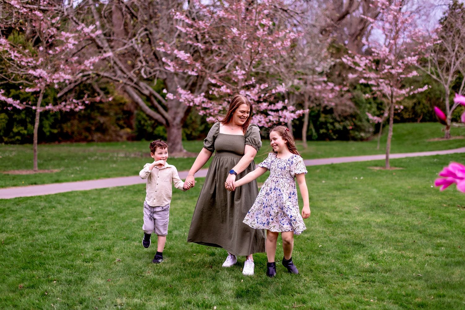 Children playing and swinging beneath blooming pink cherry blossom trees in a spring garden setting.