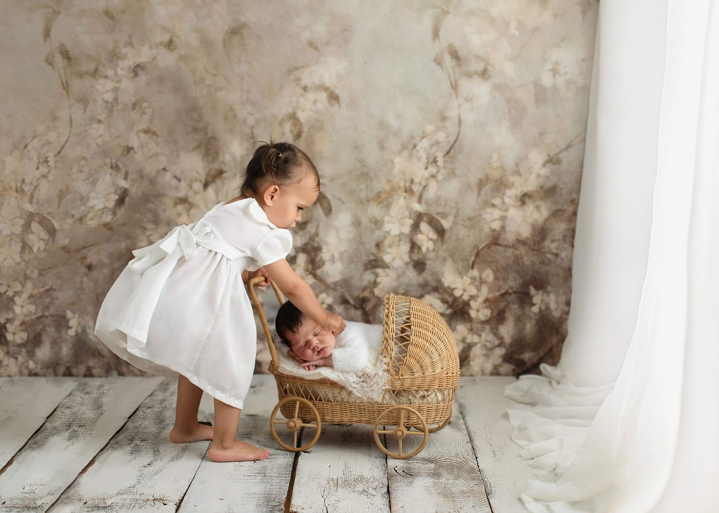 A young child in white clothing plays with a woven basket on a rustic wooden floor against a textured wall. Elizabeth Lang Photography Surre