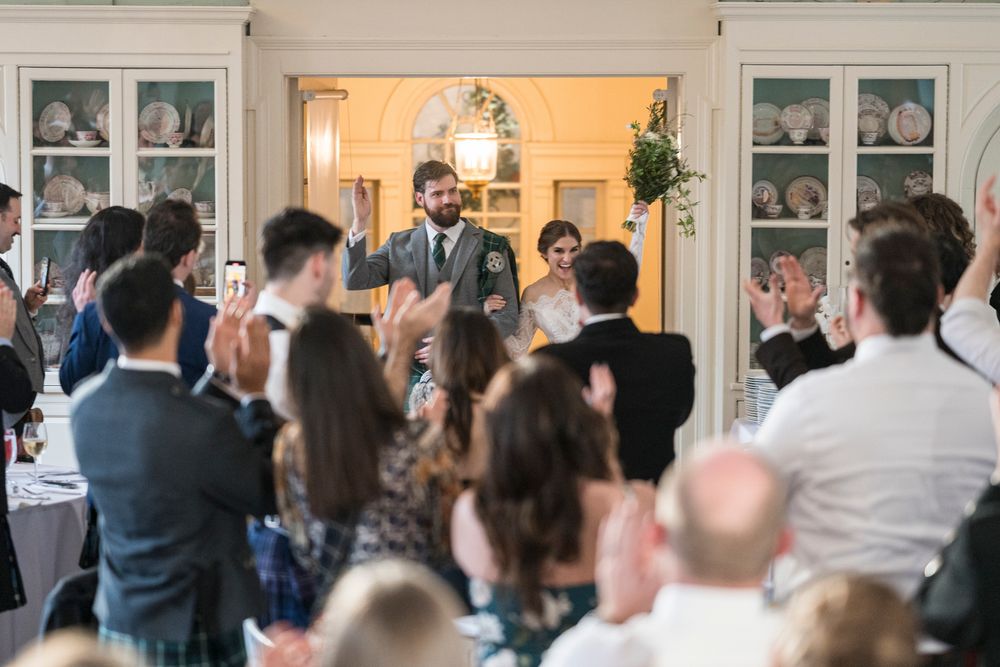 Wedding guests gather inside an elegant reception venue with white walls and display cabinets filled with china.
